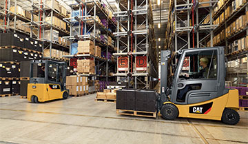 Cat pneumatic forklift moving materials in a warehouse while other forklift sits in background